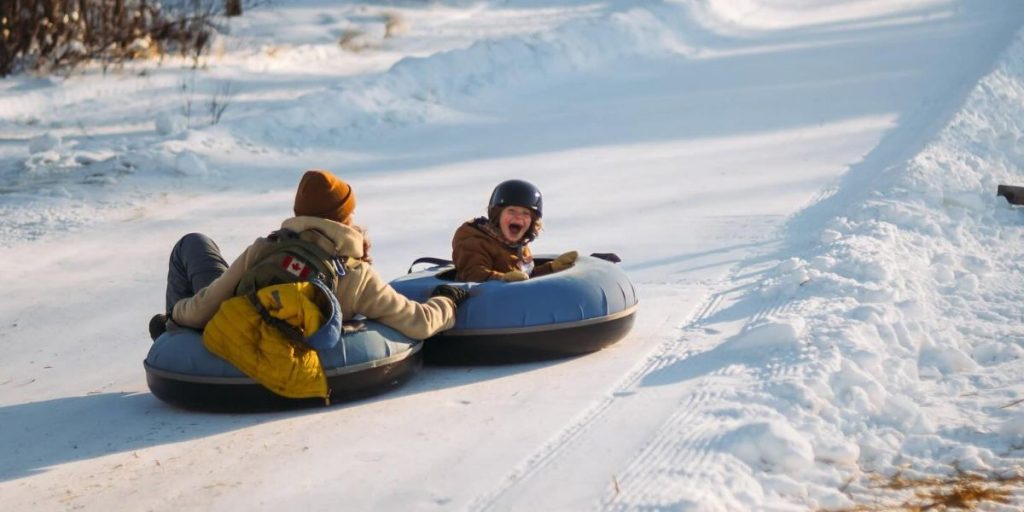 Image shows a child and parent tubing down the slopes at Falcon Ridge Ski Slopes. Falcon Ridge is home to many incredible Whiteshell winter activities.