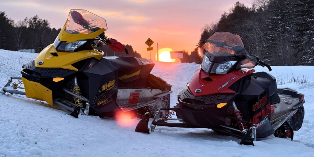 Image shows two snowmobiles parked outdoors.