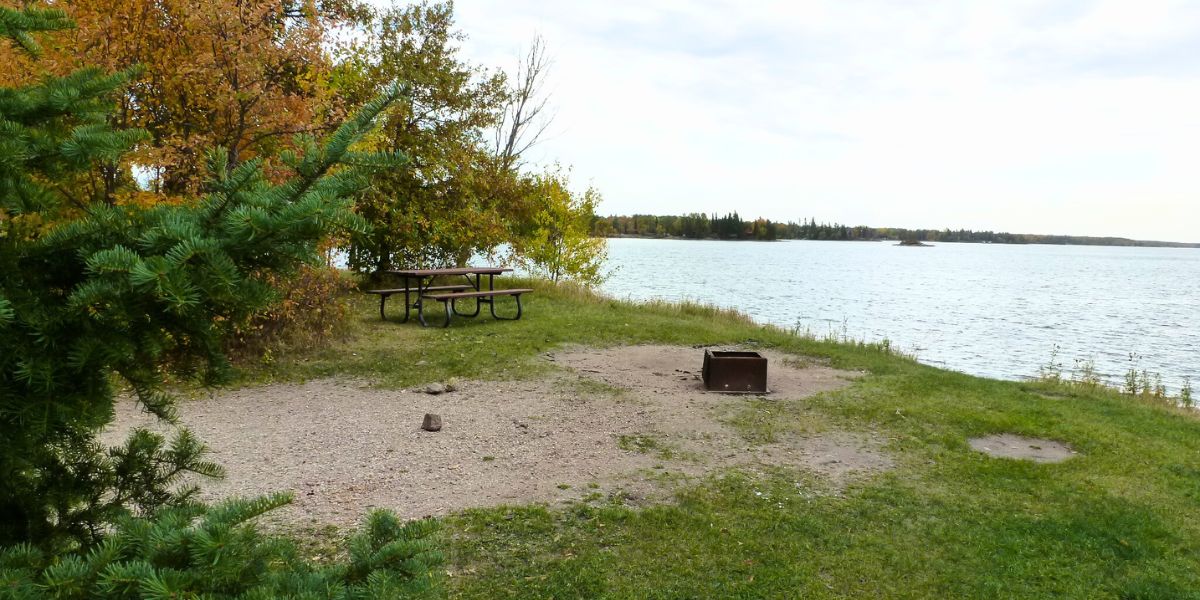 Fall campsite located right beside the water with a fire pit, showcasing that some Whiteshell campgrounds are open later in the season as well.
