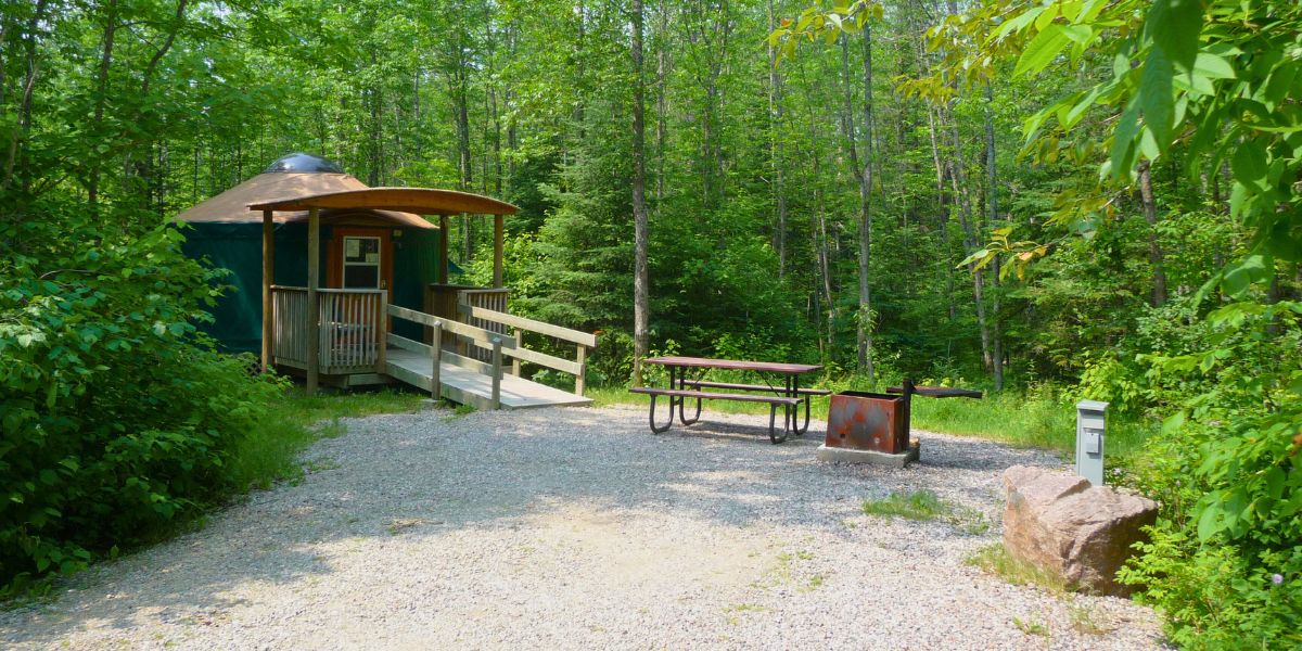 A Nutimik Yurt site with a ramp leading inside, a picnic table, and a fire pit.
